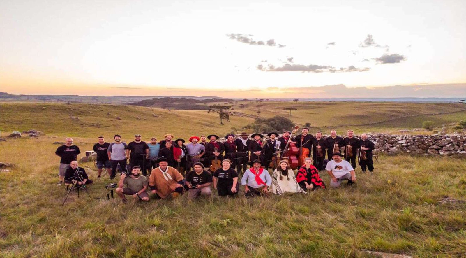 Equipe e músicos do Folcloreando reunidos no campo, no Corredor das Tropas